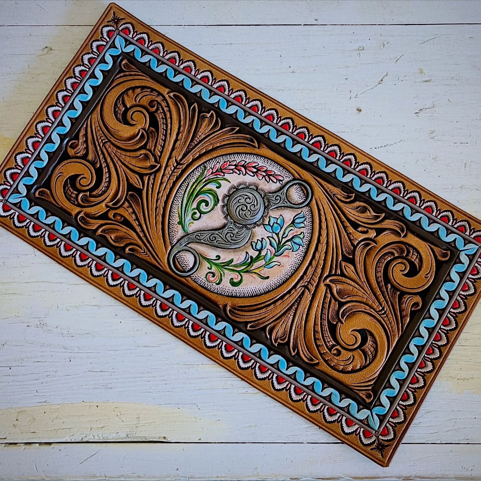 Tooled leather panel with intricate patterns and a central design on a white wooden background
