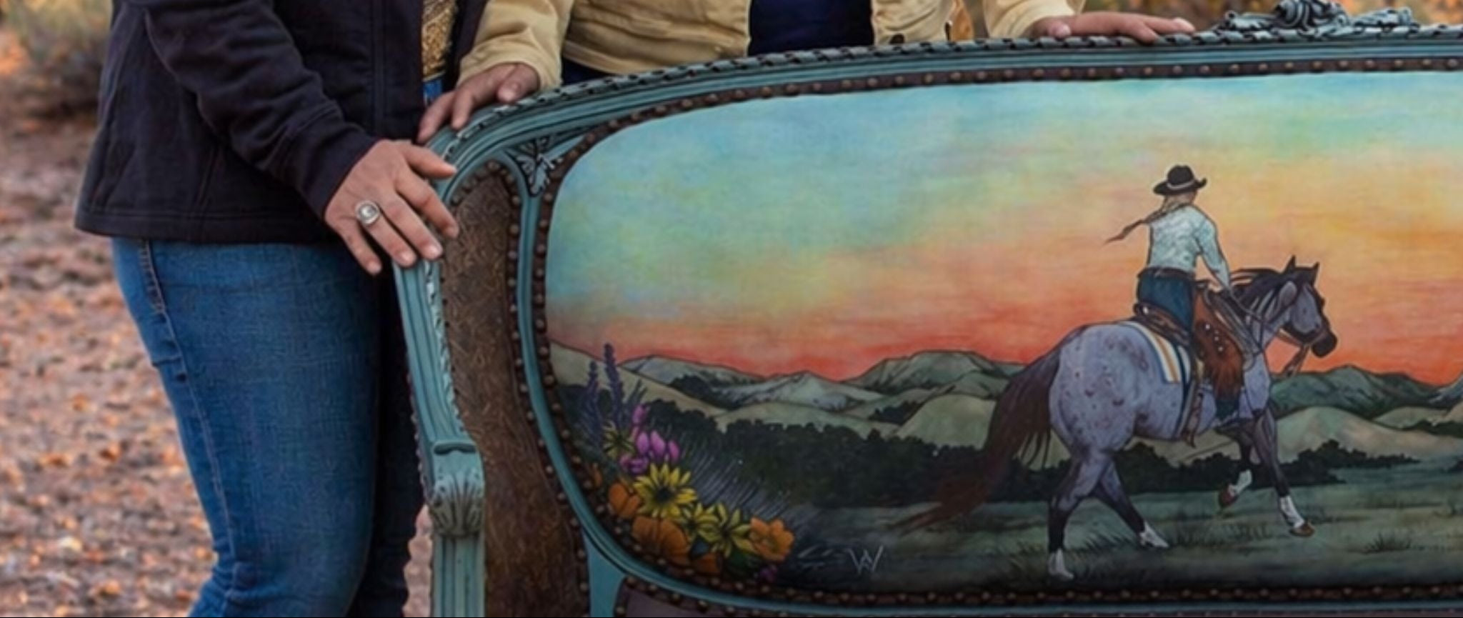 Two women standing with a painted horse trailer in a desert landscape.