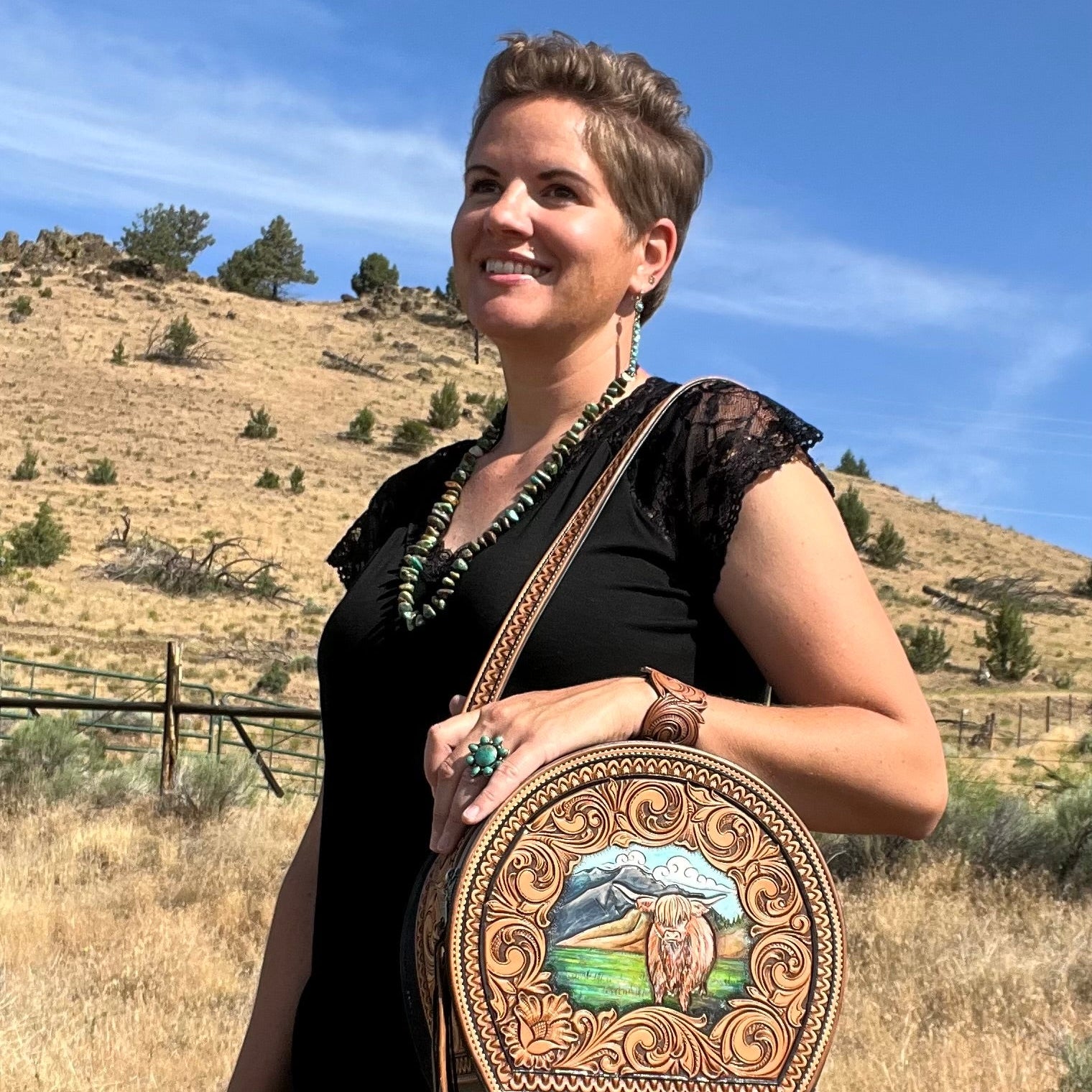 Woman holding a decorative leather bag with a scenic design in a desert landscape